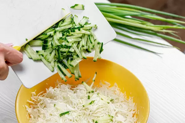 Eine weibliche Hand bereitet ein Salat mit Gurken, Frühlingszwiebel und Sauerkraut zu