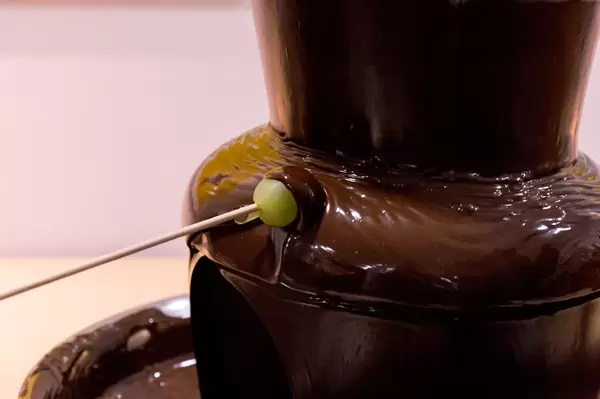 Eine Weintraube wird in einen Schokoladenbrunnen getaucht