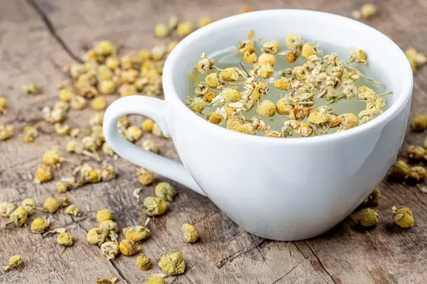 Eine weiße Tasse Kamillentee mit getrockneten Kamillenblüten auf einem hölzernen Hintergrund