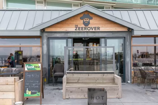 Eingang des Restaurants de Zeerover mit Außensitzplätzen, Feuerschale und hölzerner Bank