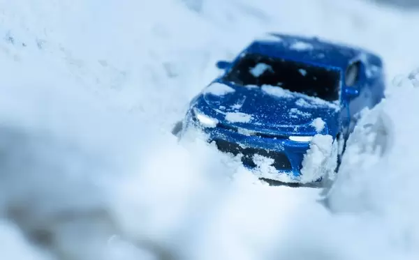 Eingeschneiter Sportwagen mit eingeschalteten Scheinwerfern