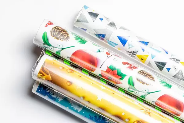 Eingeschweißte Geschenkpapier-Rollen in Weihnachtsdesign vor weißem Hintergrund Draufsicht