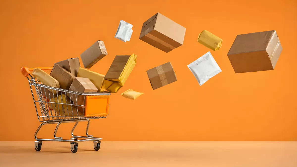 Einkaufswagen mit fliegenden Paketen auf Orangehintergrund