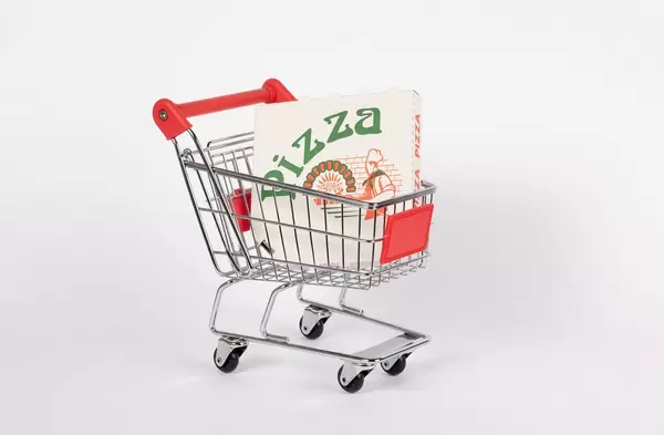 Einkaufswagen mit Pizzakarton von Lieferdienst vor weißem Hintergrund