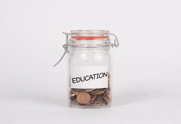 Einmachglas gefüllt mit Münzen und Beschriftung EDUDATION (Ausbildung) vor weißem Hintergrund