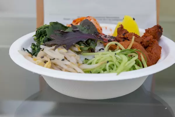 Einwegteller mit Bibimbap Bowl aus Reis mit Soja Chunks, Kimchi, Oshinko und Gemüse an Chilisoße