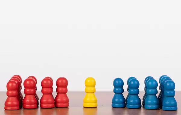 Einzelne gelbe Bauernfigur zwischen roten und blauen Spielstein-Gruppen