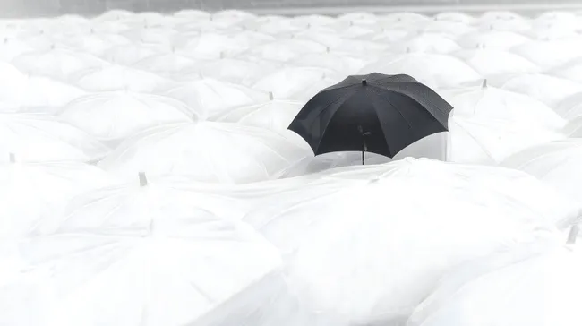 Einzigartiger schwarzer Regenschirm zwischen weißen Schirmen