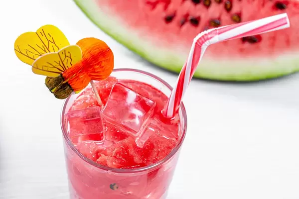 Eisgekühlter Wassermelonen-Smoothie mit Strohhalm vor Melonenschnitz auf weißem Tisch