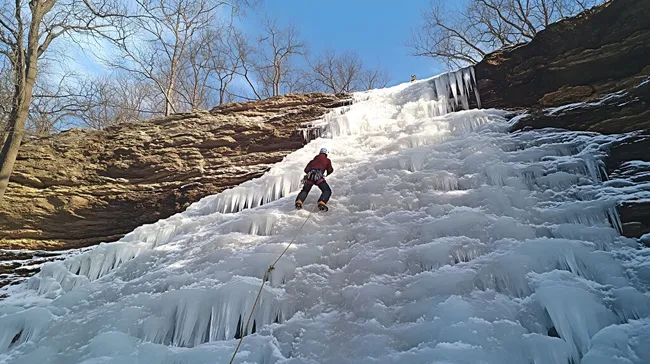Eiskletterer erklimmt gefrorenen Wasserfall im Winterwald