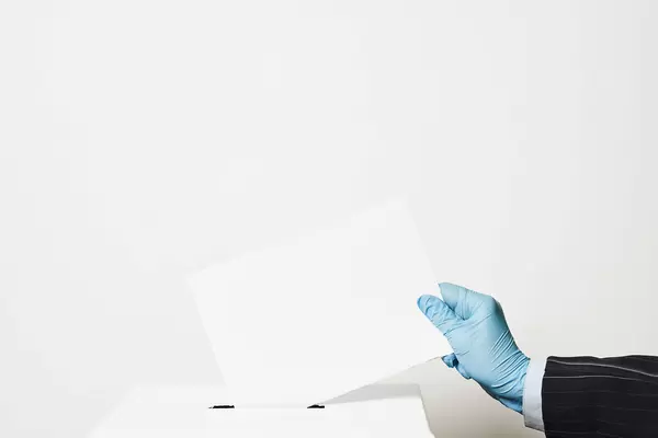 Election during Covid-19 pandemic. A person in protective gloves throwing paper into the ballot box