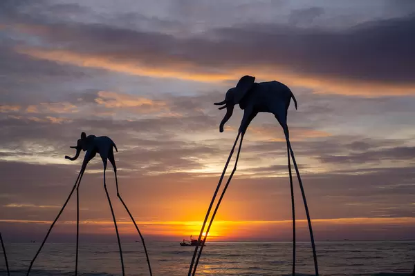 Elefanten auf Stelzen als Touristenattraktion am Sunset Sanato Beach Club bei Sonnenuntergang mit Fischerboot im Hintergrund in Phu Quoc, Vietnam