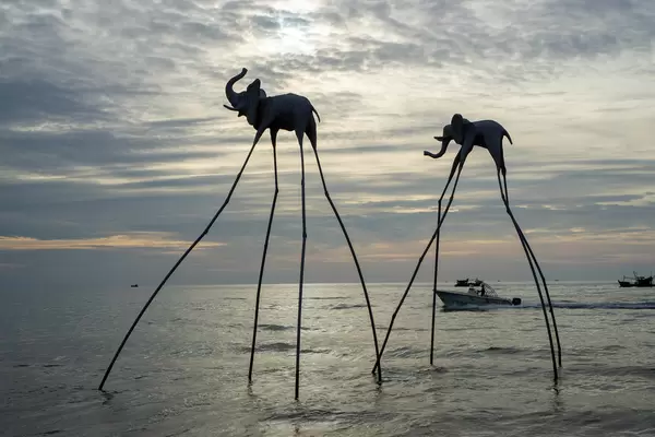 Elefanten Skulpturen auf langen Stelzen im Meer mit Fischerbooten und Motorboot im Hintergrund bei Sonnenuntergang in Phu Quoc, Vietnam