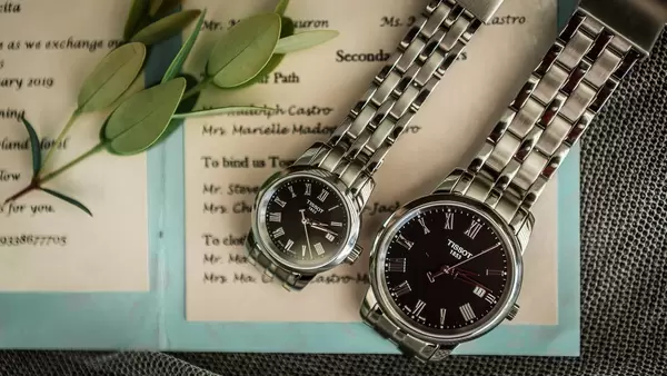 Elegante, silberne Uhren von Tissot im Partnerlook liegen mit Blättern auf Hochzeitseinladung