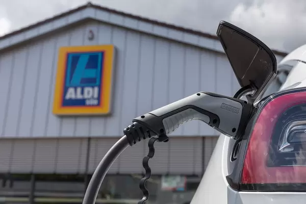Elektroauto laden: Tesla Model 3 mit einem Typ 2 Ladestecker, tankt Sonnenenergie vor dem Aldi-Süd Supermarkt