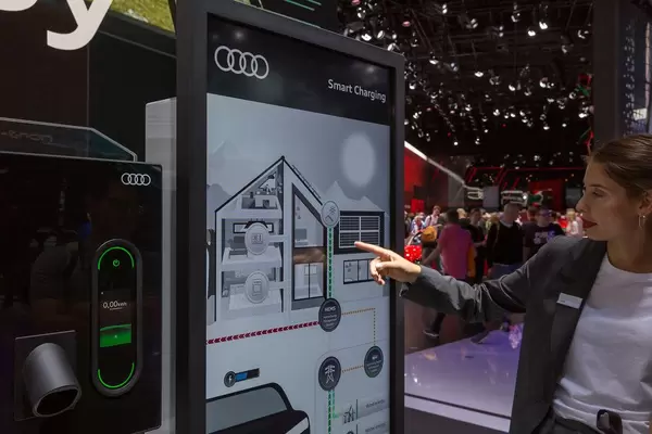 Elektroauto und Smart Home vernetzen: Frau zeigt auf das Home Energy Management System von Audo Smart Charging Ladesystem