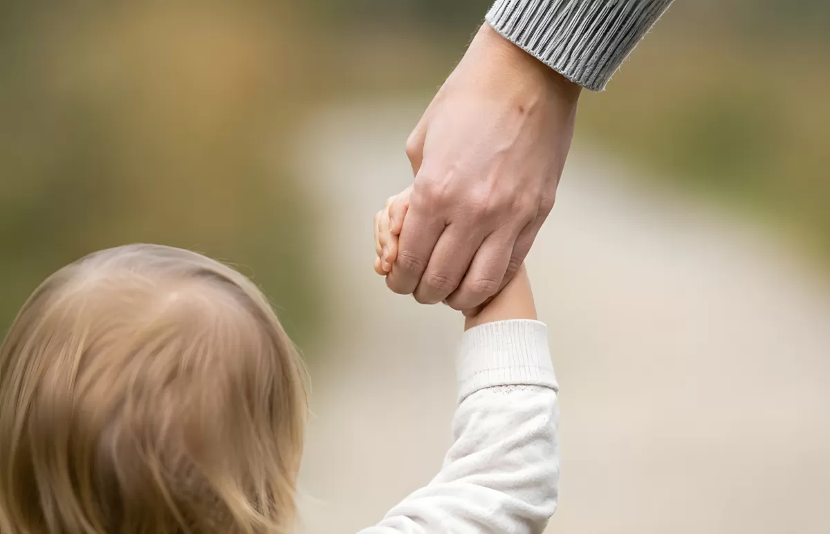 Elternteil hält Kind an der Hand im Freien