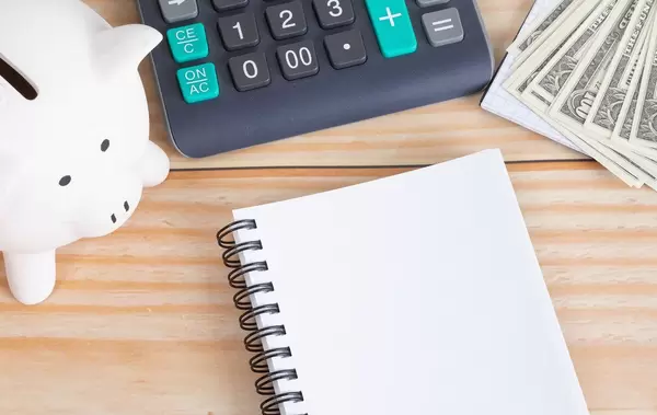 Empty notebook with piggy bank, calculator and money on table