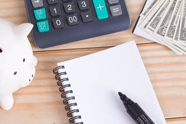 Empty notebook with piggy bank, calculator and money on wooden table