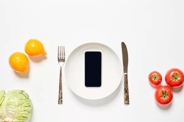 Empty plate with mobile phone and fresh tomatoes, lemons and cabbage