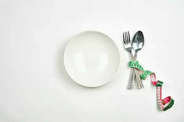 Empty white plate with a spoon and fork wrapped in measuring tape on white background. Diet concept