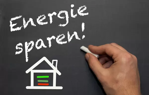 Energie sparen!: Weiße Handschrift mit gezeichnetem Strich-Haus aus Kreide auf schwarzer Tafel - Nahaufnahme