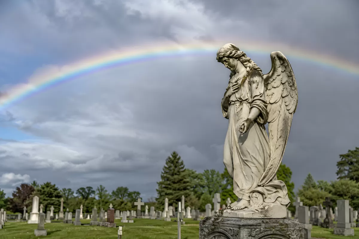Engelsstatue auf Friedhof mit Regenbogen am Himmel