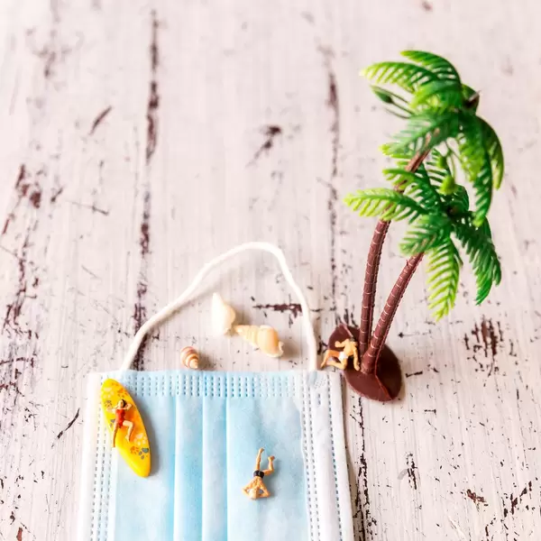 Enjoying a holiday despite the Covid-19 pandemic. Face mask with figures swimming and sunbathing