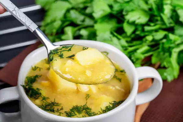 Erbsensuppe mit Kartoffeln und Dill auf einem Löffel und in einer weißen Suppetasse Nahaufnahme
