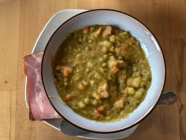 Erbsensuppe mit Stück Schinken auf Holztisch