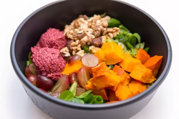 Erntedank Bowl mit Hummus aus roter Beete, Feldsalat, warmer Curry Quinoa, gerösteter Hokkiado Kürbis, rote Trauben, jungem Lauch, Walnusskernen und Joghurt-Orangen-Dip