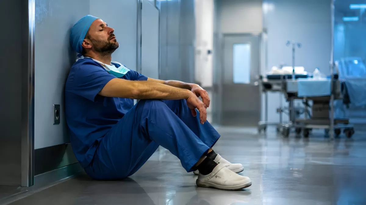Erschöpfter Arzt sitzt auf dem Boden im Krankenhausflur