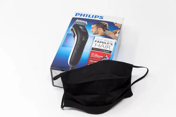 Essentials for the Covid-19 era: a black face mask and hair clipper Philips QC5115/15 on a white background