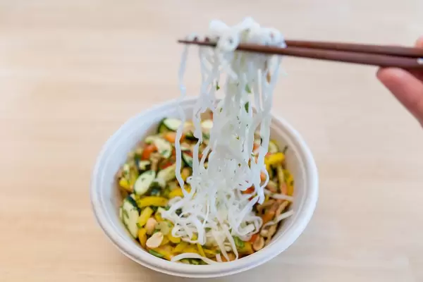Essstäbchen halten Nudeln über Gemüsepfanne mit Kräutern und Erdnüssen