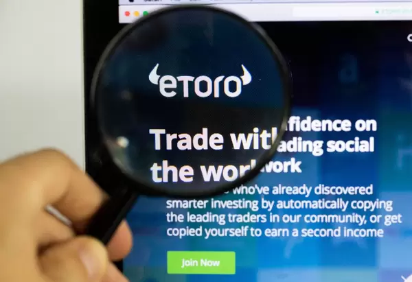 Etoro-Logo am PC-Monitor, durch eine Lupe fotografiert