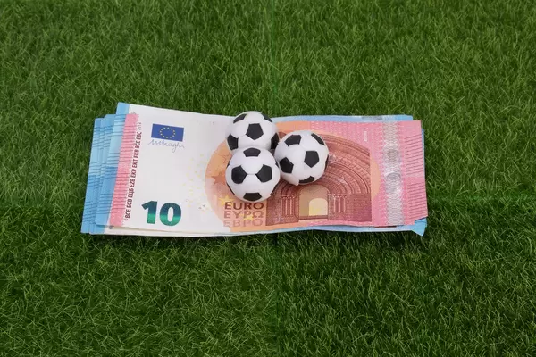 Euro banknotes with soccer balls on green grass