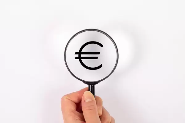 Euro Zeichen hinter Leselupe vor weißem Hintergrund