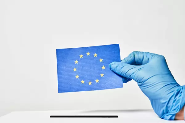 Europa, Wahl und Covid-19: Hand mit Einweghandschuh wirft EU-Zettel in die Wahlurne ein