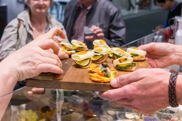 Exhibition chef hands over finger food on a wooden board to IFA fair visitors