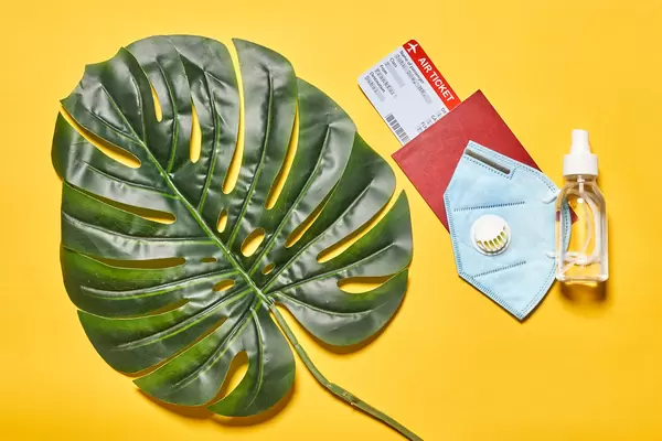 Face mask, antiseptic gel and tickets in passport on yellow background. New normal concept.