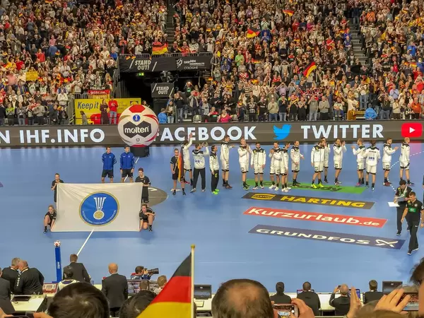 Fahne der International Handball Federation auf Handballfeld vor Deutscher Mannschaft
