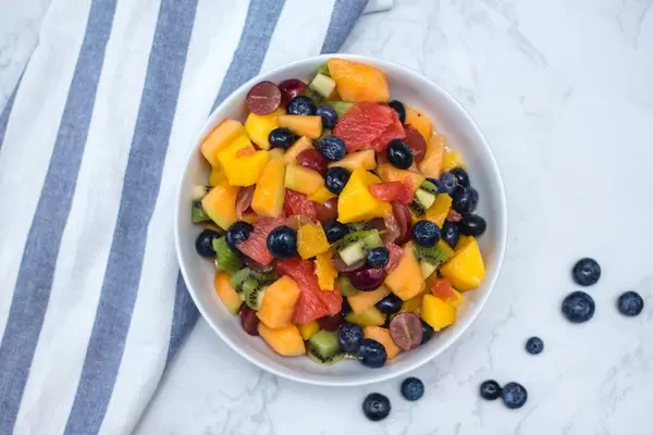 Farbenfroher Obstsalat mit Beeren, Mango, Melone und Kiwi, auf einem Küchentisch