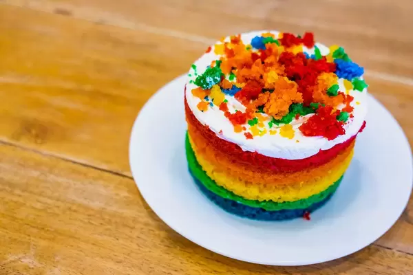 Farbenfroher Regenbogenkuchen mit Buttercreme auf Teller auf Holztisch