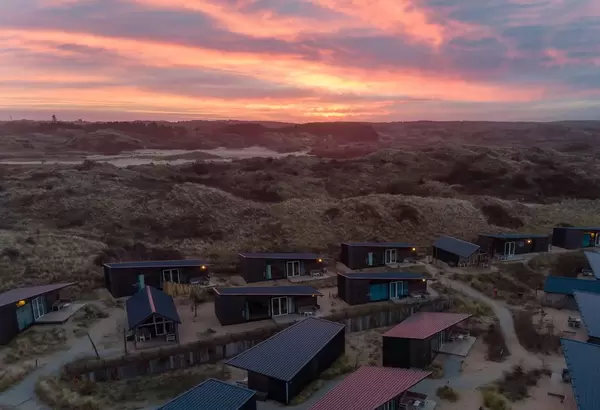 Farbenfroher Sonnenuntergang über grünen Hügeln in den Niederlanden mit Ferienchalets im Vordergrund
