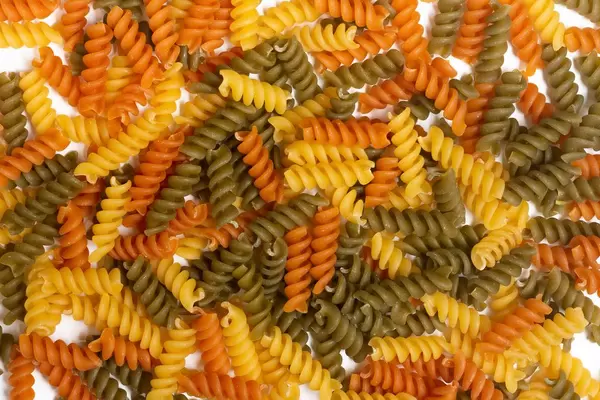 Farbige Fusilli Pasta ungekocht in gelb, orange und grün auf weißem Holztisch verteilt