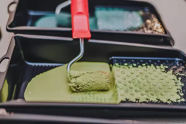 Farbschale mit Farbrolle in grüner Wandfarbe mit zweiter Schale im Hintergrund