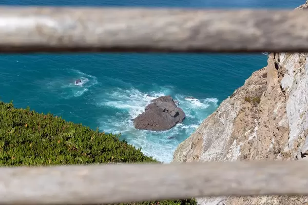 Felsen im türkisblauen Ozean vor der Küste von Cabo da Roca mit Essbarer Mittagsblume im Vordergrund