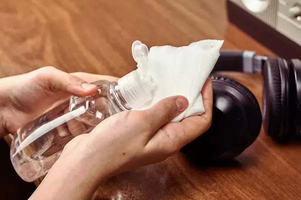 Female applying disinfectant onto wipe for cleaning headphones