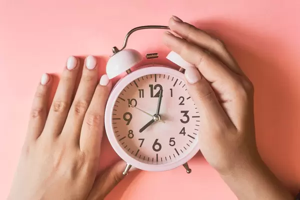 Female checking a time. Woman hands taking an alarm clock