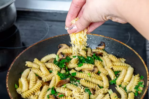 Female hand adds cheese to a pasta pan (Flip 2019)